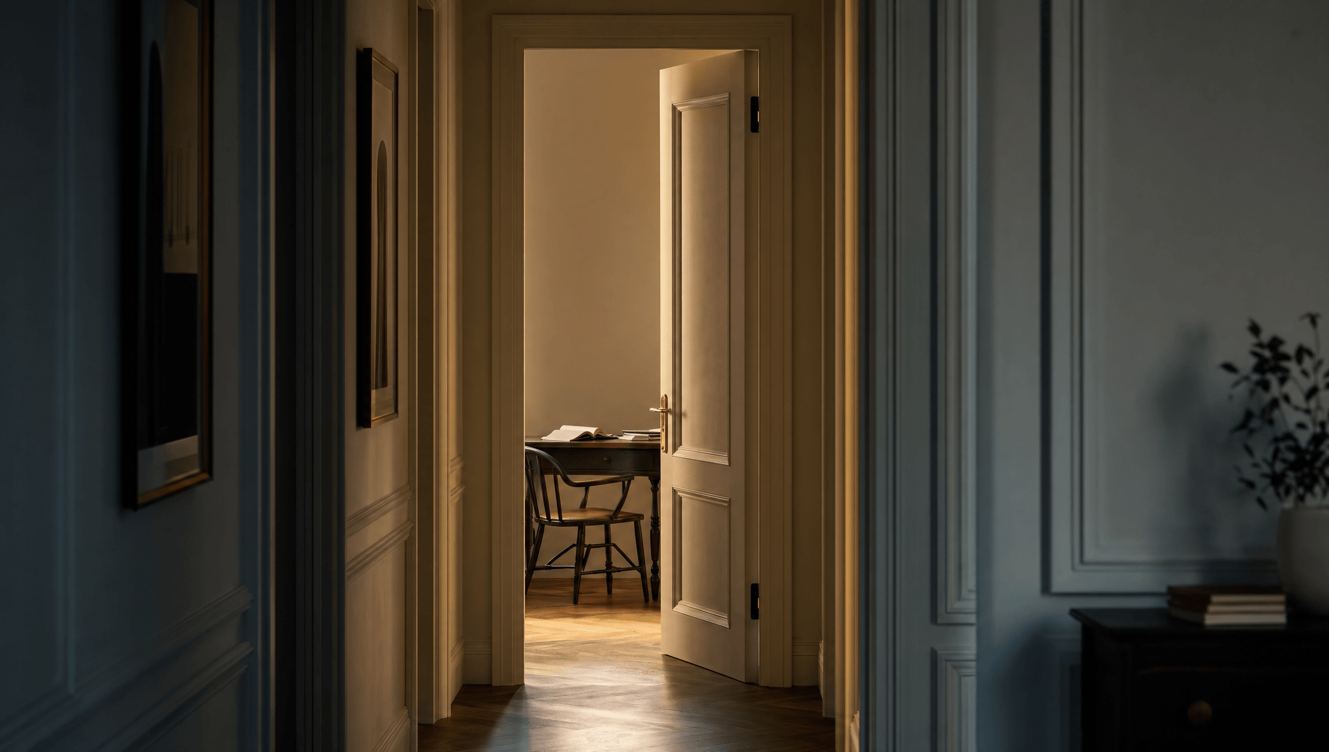 A single open door at the end of a softly-lit corridor, brass handle catching warm light, a desk and chair just visible in the room beyond.