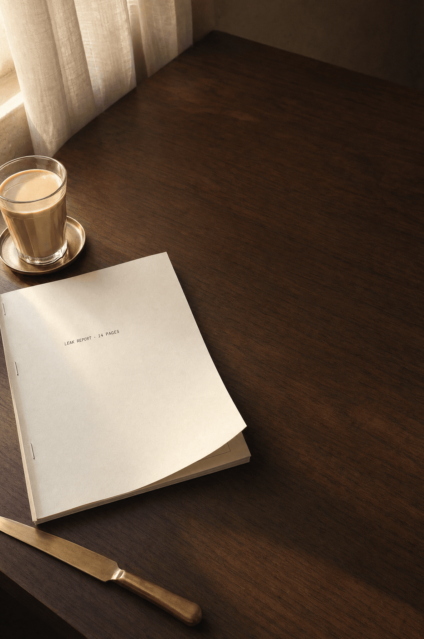 Bound leak report on a walnut desk, beside a brass paper-knife and a glass of karak chai