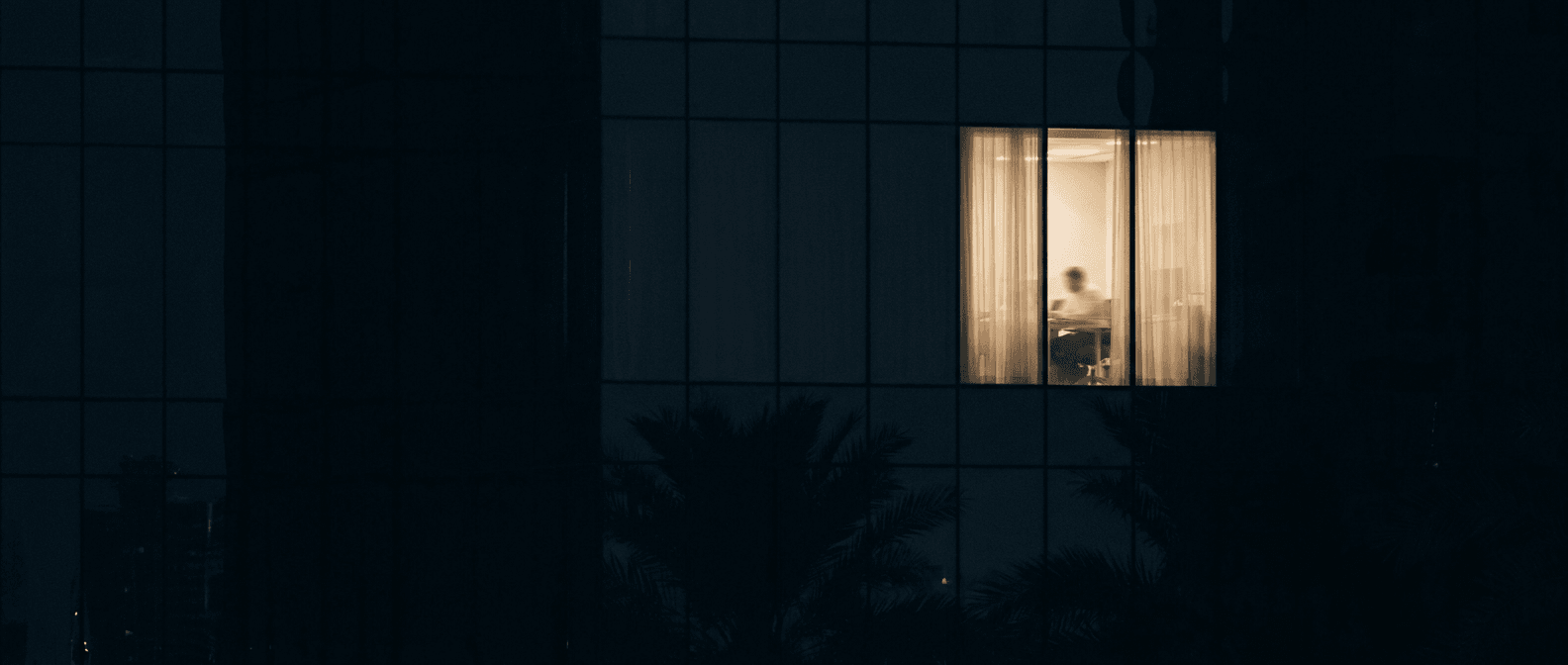 A single warmly-lit window in a Dubai office at night — the clinic is awake while the city sleeps
