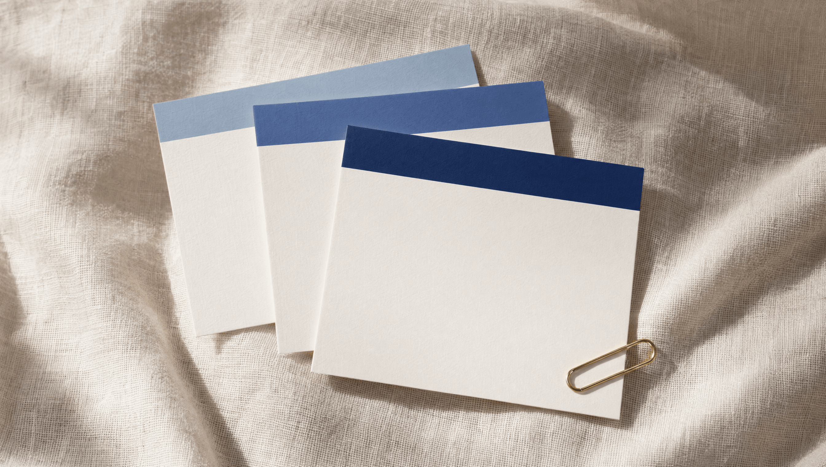 Three cream printed cards arranged in a fan, each with a different ink-blue category band at the top, brass paperclip at the corner.
